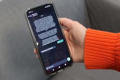 Hand, die aus orangenem Pulli ragt, hält Smartphone mit MetaAI in der Hand