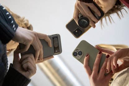 Blick von unten: Drei Personen gucken auf ihre Smartphones.
