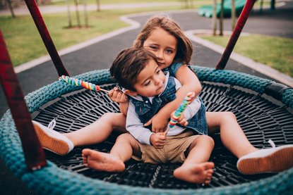 Zwei Kinder sitzen in einer Nestschaukel und halten Lollies.