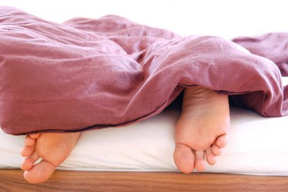 Füße hängen unter roter Bettdecke aus dem Bett